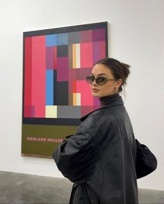 a woman wearing sunglasses standing in front of a colorful painting on the wall with her back turned to the camera