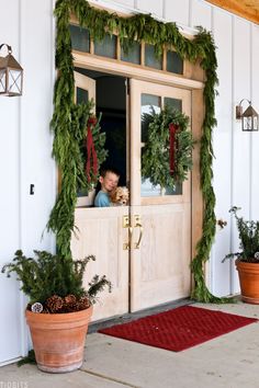 two potted plants are sitting on the front porch with christmas wreaths hanging over them