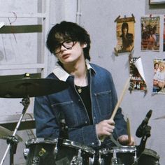 a young man playing drums in front of a wall with pictures on it and posters behind him