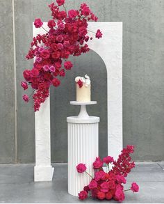 a white vase with flowers and a cake on the top is surrounded by red flowers