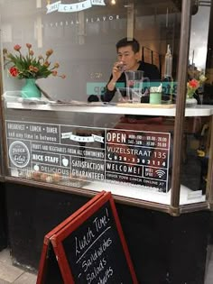 a man sitting at a table in front of a restaurant with a menu written on it