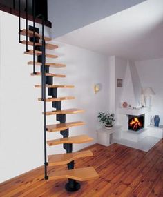 there is a spiral staircase in the middle of this living room with wood floors and white walls