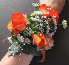 a woman's arm with orange flowers and greenery on it, while wearing a wrist corsage