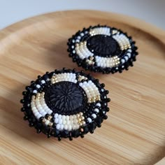 two black and white beaded earrings sitting on top of a wooden tray