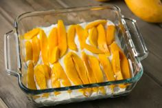 a glass casserole dish filled with mangoes and yogurt on a wooden table