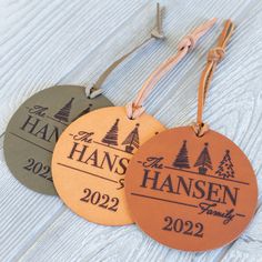 three personalized ornament hanging from string on wooden table with pine trees in the background