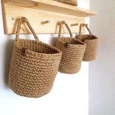 three woven baskets hanging from a wooden hook on a white wall with hooks in it