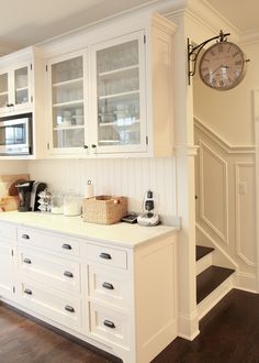 a kitchen with white cabinets and wooden flooring next to a clock on the wall