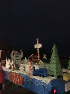 people are walking around in front of a fake christmas village at night with lights and decorations