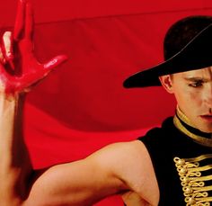 a man wearing a black hat and holding his hand up in the air with red paint on it