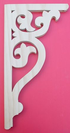 a white wooden shelf bracket on a pink background with the letter s carved into it