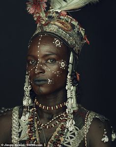 an african woman with painted face and feathers on her head, wearing beaded jewelry