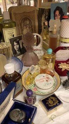 a table topped with lots of different types of perfumes and personal care items on top of a white cloth covered table