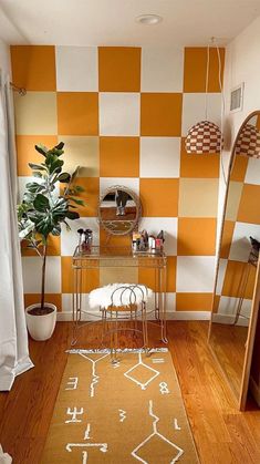 an orange and white checkered wall in a small room with a mirror, stools, rug and potted plant