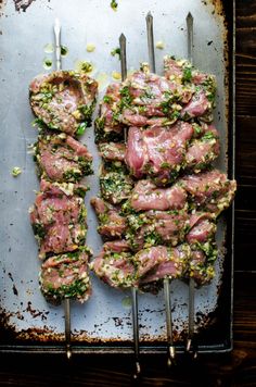 meat skewers with herbs and seasonings on a baking sheet