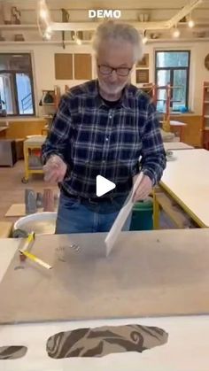 an older man standing in front of a table cutting something with a pair of scissors