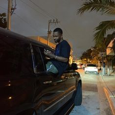 a man sitting on the hood of a car looking at his cell phone