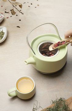 a person holding a wooden spoon over a cup of tea on top of a table