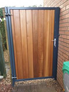 a wooden gate is open on the side of a brick building with a trash can next to it