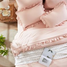 a bed with pink sheets and pillows on top of it next to a potted plant