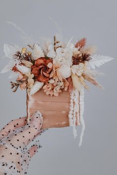 a person holding a bag with flowers and feathers on it in front of a gray background