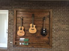 three guitars are hanging on the wall in front of a brick wall with an open window