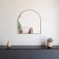 a mirror on the wall above a dresser with a potted plant in front of it