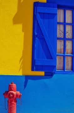 a red fire hydrant in front of a blue and yellow wall with a window