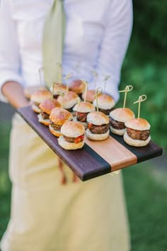 a person holding a tray with mini burgers on it