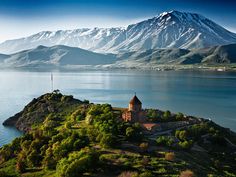 an island with a church on it in the middle of water and mountains behind it