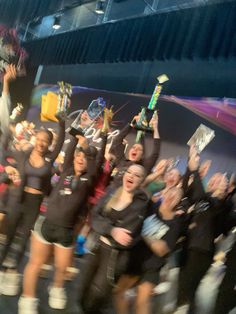 a group of cheerleaders standing in front of a stage with their arms up