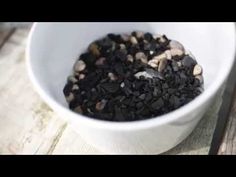 a white bowl filled with lots of black and brown rocks next to a knife on top of a wooden table