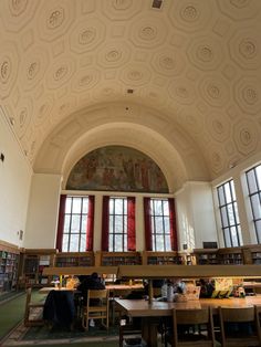 an empty library filled with lots of books and desks next to large red windows