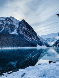 a lake surrounded by snow covered mountains under a cloudy sky