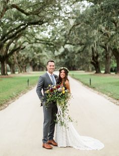 a bride and groom standing on a dirt road in front of trees