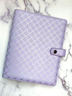 a purple and white patterned notebook sitting on top of a marble counter with a button in the middle