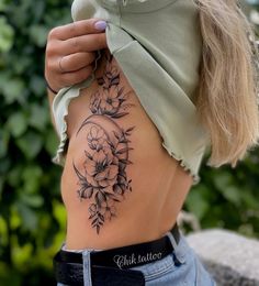 a woman's lower back tattoo with flowers and leaves on her stomach, in front of some bushes