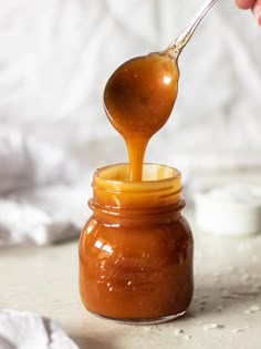 a spoon full of caramel sauce being poured into a jar