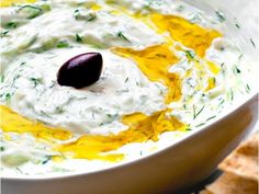 a white bowl filled with dip next to crackers and an olive on the side