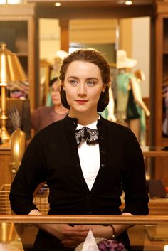 a woman standing in front of a store counter wearing a bow tie and black cardigan