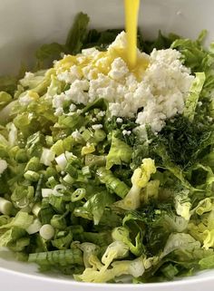 a bowl filled with lettuce and cheese being poured into it