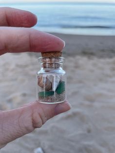 a hand holding a tiny bottle filled with sand and sea shells