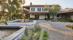 a house with a fountain in front of it and landscaping around the pool area on either side