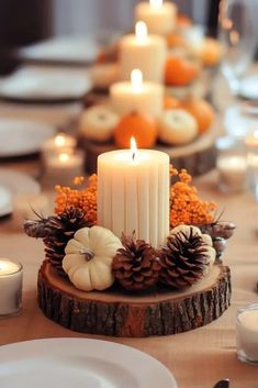 a table with candles, pine cones and pumpkins on it's centerpiece