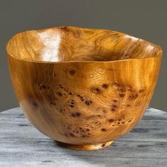 a wooden bowl sitting on top of a marble table next to a gray wall and floor