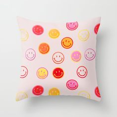 a pink pillow with colorful smiley faces printed on the front and back, along with white background