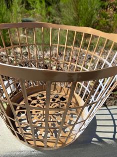 a large metal basket sitting on top of a cement floor next to grass and bushes