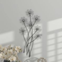 a vase filled with white flowers sitting next to a metal wall art set on top of a table