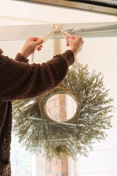 a woman is hanging a wreath on the front door with a pair of scissors to tie it