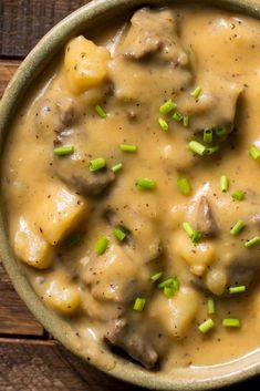 a bowl filled with meat and gravy on top of a wooden table